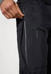 Μαύρο εξωτερικό παντελόνι με εμφανή πλευρικό φερμουάρ, λεία υφή και ενισχυμένες ραφές. Περιλαμβάνει επιπλέον τσέπη με φερμουάρ.