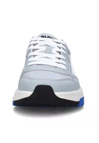 Sneaker grigia e bianca con una parte superiore testurizzata, lacci bianchi, suola elevata nera e blu, caratterizzata da un design minimalista e senza marchi prominenti.