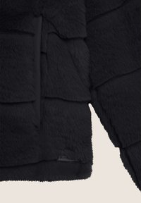 Giacca nera in pelliccia sintetica con un design texturizzato a strati e una tasca frontale elegante. Materiale morbido con una leggera lucentezza e un'etichetta con marchio.