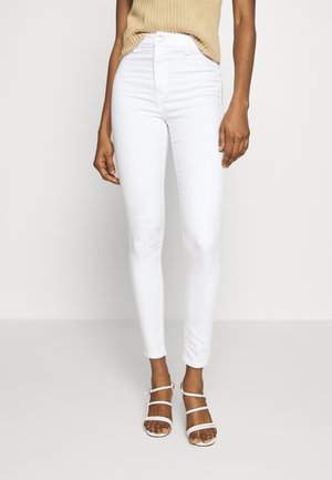 Jeans blancos de talle alto con una textura suave y un diseño ajustado, combinados con sandalias blancas de tiras. Arriba se ve un top de punto beige.