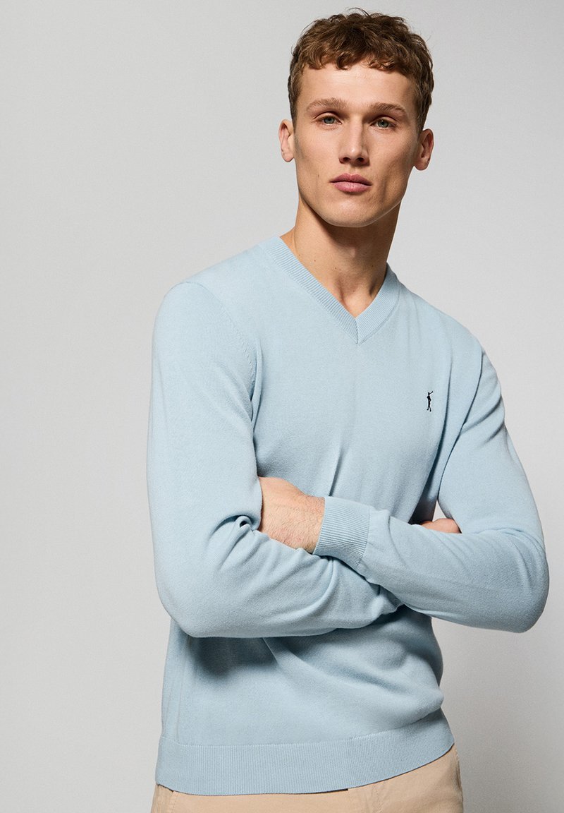 Jasnoniebieski sweter z dekoltem w kształcie litery V, wykonany z miękkiego materiału, z prążkowanymi mankietami i dołem. Mały logotyp na piersi. Klasyczny krój i długie rękawy.