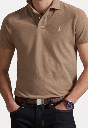 Bruin polo shirt met korte mouwen en een tweeknoopsluiting. Heeft een geborduurd logo op de borst en een gestructureerde stof. Gekocht met een bruine riem en horloge.