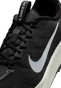 Svart träningssko med texturerat tygovandel, med en framträdande vit Swoosh-logotyp, svarta snören och en dragflik märkt "NIKE WILDHORSE 10."