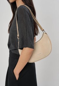 Borsa a tracolla in suede beige con una forma curva e dettagli in argento. Design minimalista con chiusura a zip.