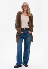 Bruine gebreide cardigan, crèmekleurige top, wijde blauwe denim jeans, bruine riem met zilveren gesp en chunky zwarte schoenen. Elegante, casual outfit.