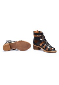 Sandalias de tacón de cuero negro con diseño recortado, acentos de cuero marrón y suela texturizada. Presenta un cierre lateral con cremallera y tacón apilado.