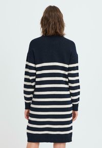 Marineblå og kremfarget stripete strikkekjole med lange ermer, rund hals og avslappet passform, med brede horisontale striper og ribbestrikkede mansjetter.