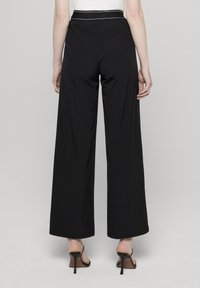 Svarte vidbukse med glatt tekstur, høy midje og hvit aksentdetalj. Stylet med svarte hælsandaler.