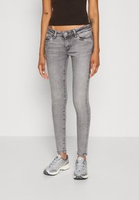 Modelo femenina que lleva jeans de mezclilla gris ajustados con un acabado desgastado, combinados con zapatillas deportivas plateadas. Tejido suave, silueta esbelta.