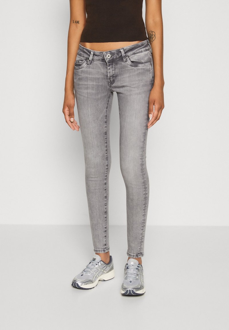 Modelo femenina que lleva jeans de mezclilla gris ajustados con un acabado desgastado, combinados con zapatillas deportivas plateadas. Tejido suave, silueta esbelta.