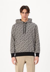Black and white patterned hoodie with a drawstring hood, ribbed cuffs, and a kangaroo pocket, worn over light-colored pants.