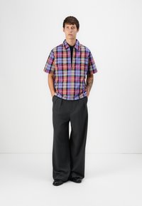Short-sleeve plaid shirt with blue, purple, and pink tones, featuring a collar and chest pockets, paired with wide grey trousers and black shoes.