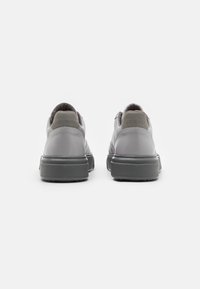 Graue Leder-Sneaker mit einem strukturierten Design, ausgestattet mit einer kontrastierenden dunklen Gummisohle und geprägtem Branding an der Ferse.