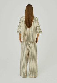 Gestreept tweedelig outfit in beige met verticale zwarte strepen. Bevat een top met korte mouwen en broek met wijde pijpen, gemaakt van lichtgewicht stof.