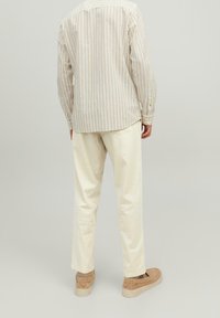 Light beige striped long-sleeve shirt, cream-colored trousers, and beige slip-on shoes. Soft texture, relaxed fit, and minimal detailing.