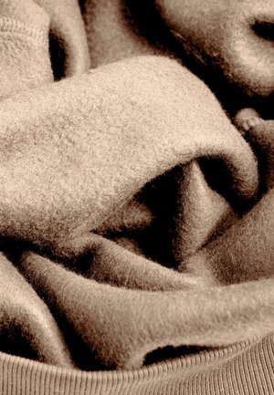 Beige wollen stof met een zachte textuur, gelaagd en gevouwen, met subtiele kleurvariaties en een geribbelde rand aan de onderkant.