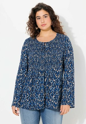 Vloeiende blauwe top met patroon, voorzien van lange mouwen, een smocked lijfje en een keyhole-detail bij de halslijn. Textuurstof met lichte accenten.