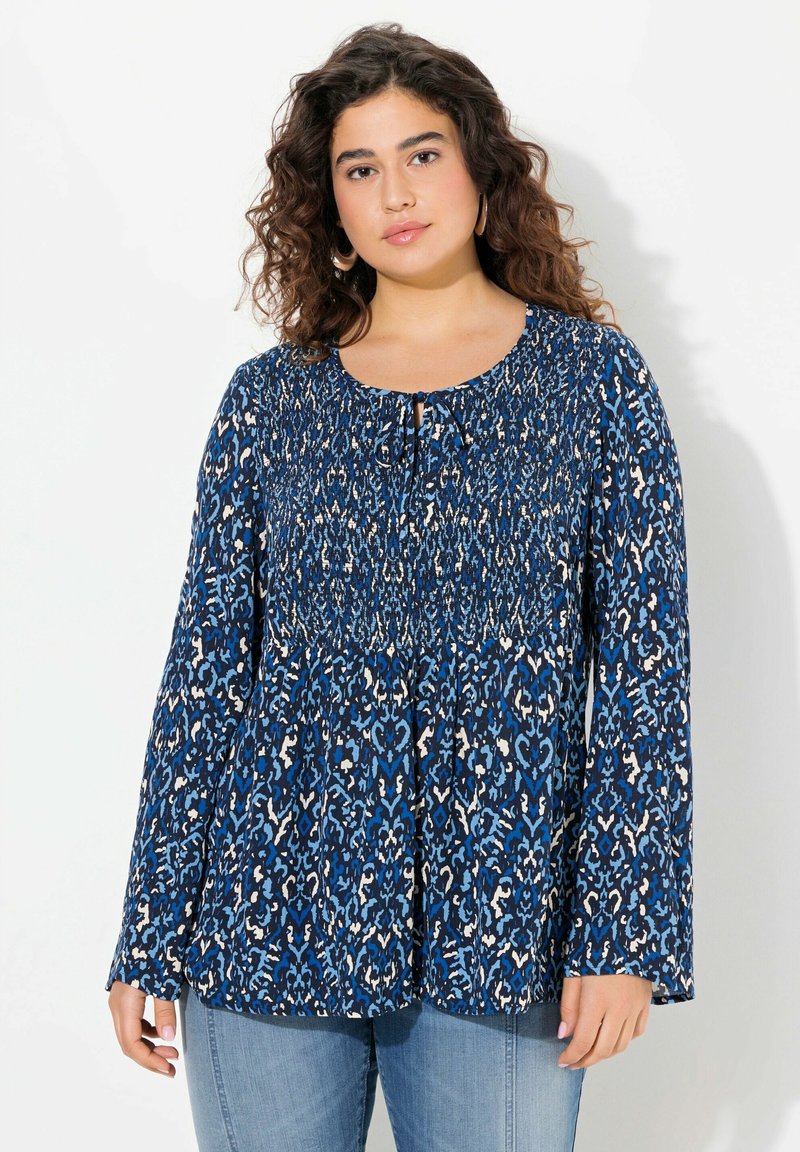 Top fluido blu con motivo, caratterizzato da maniche lunghe, corpetto smockato e un dettaglio a chiave nel colletto. Tessuto testurizzato con leggeri accenti.