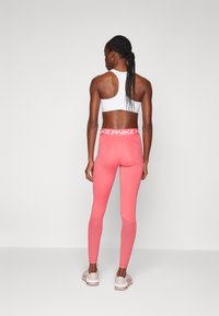 Roze leggings met een aansluitend ontwerp en elastische tailleband, gecombineerd met een witte sportbeha met racerback, beide gemaakt van rekbaar materiaal.