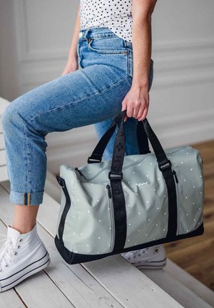 Gray duffle bag with white polka dots, black straps, and hardware. The bag features a zipper and a soft, textured surface.