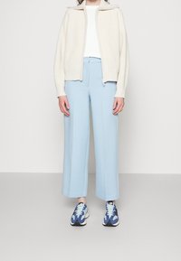 Kermainen ribbineulottu vetoketjullinen neuletakki, valkoinen toppi, vaaleansiniset leveälahkeiset housut ja siniset kuvioidut lenkkarit. Sileä kangas, jossa selkeä rakenne.