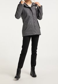 Person wearing a dark gray hooded rain jacket with front pockets, black pants, and black lace-up ankle boots, posing against a neutral background.