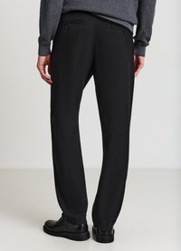 Schwarze Hosen aus strukturiertem Stoff, mit zwei Gesäßtaschen, einem geraden Bein und kombiniert mit schwarzen Schnürschuhen.