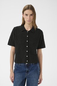 Črna bluza s kratkimi rokavi iz teksturirane tkanine, z ovratnim izrezom in zapiranjem na sprednji strani s perlami. Oblečena s kavbojkami z visokim pasom.