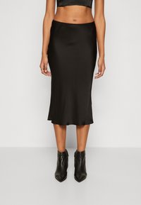 Schwarzer Satin-Midirock mit glatter Textur, figurbetontem Schnitt und abgerundetem Saum, kombiniert mit schwarzen Leder-Stiefeletten.