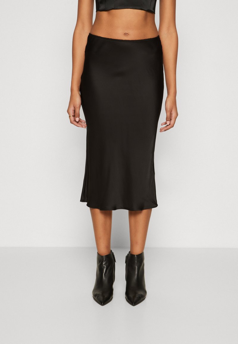 Schwarzer Satin-Midirock mit glatter Textur, figurbetontem Schnitt und abgerundetem Saum, kombiniert mit schwarzen Leder-Stiefeletten.