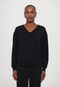 Čierny sweatshirt s V-výstrihom, priliehavým spodným lemom a dlhými rukávmi. Má textúrované logo na ľavej hrudi a hladkú štruktúru po celom povrchu.
