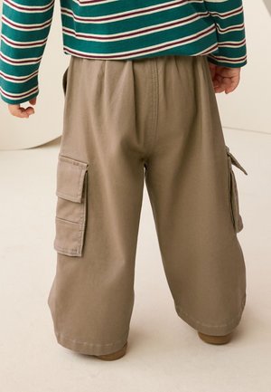 Bambino che indossa pantaloni cargo kaki a gamba larga con tasche a patta e una maglia a maniche lunghe a righe verdi, bianche e rosse, in piedi all'interno.