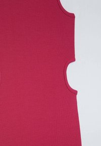 Gros plan d'un haut sans manches côtelé rose foncé montrant les détails de l'emmanchure et de la couture d'épaule sur un fond clair.