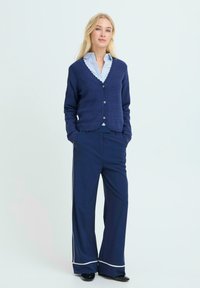 Námořnický kardigan s texturovaným pletením, s výstřihem do V a zapínáním na knoflíky, v kombinaci s širšími námořnickými kalhotami s bílými detaily.