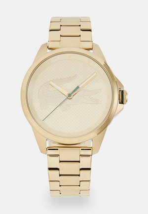 Gold watch with linked metal band, round face, and textured cream dial featuring a crocodile logo and contrasting hour markers and hands.