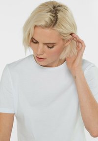 Weißes Baumwoll-T-Shirt mit klassischem Rundhalsausschnitt, kurzen Ärmeln, glatter Textur und lässiger Passform, prominent an einer Person präsentiert.