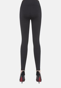 Czarne legginsy o gładkiej fakturze z wysokim stanem, połączone z czarnymi szpilkami z czerwonymi podeszwami. Widok od tyłu.