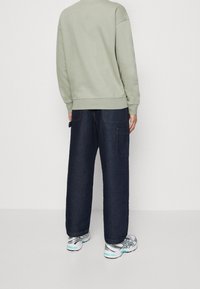 Lichtgroene sweatshirt met een ronde hals; gecombineerd met donkerblauwe jeans met wijde pijpen, voorzien van zijzakken en zichtbare stiksel details.