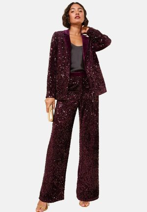 Kastanienroter Paillettenanzug mit taillierter Jacke und weit geschnittenen Hosen, ergänzt durch ein schwarzes Oberteil und eine goldene Clutch. Glatte und reflektierende Textur.
