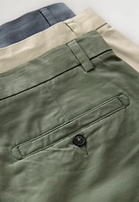 Trei perechi de pantaloni în verde, bej și gri, având un buzunar pe spate cu un nasture negru și un material neted, texturat.