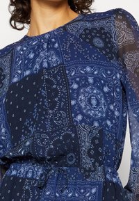 Navyblaues Kleid aus leichtem Stoff, das mit einem Paisleymuster in verschiedenen Farbtönen und Texturen versehen ist und über eine verstellbare Taillenpartie verfügt.