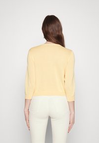 Gul cropped sweater med trekvartærmer, glat tekstur og runde hals. Sammen med lystfarvede tætsiddende bukser.