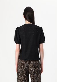 Zwarte textuurtop met pofmouwen, voorzien van een ingewikkeld patroon. Gekleed met bruine broek met luipaardprint, met een ontspannen pasvorm.