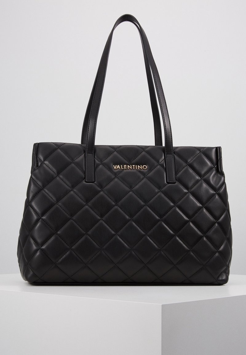 Sac fourre-tout en cuir noir matelassé avec deux longues poignées et le logo doré "VALENTINO" sur le devant. Présente une forme structurée et une texture lisse.