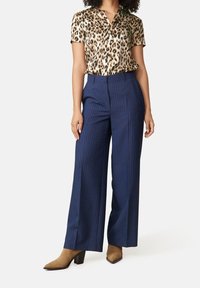 Leopardmönstrad silkesblus med korta ärmar, matchad med marinblå rutiga vida byxor. Bruna klackstövlar kompletterar outfiten.