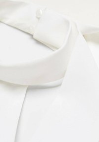 Bluză albă cu o textură netedă și moale. Dispune de un guler structurat și două butoane mici la gât. Design simplist și curat.