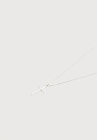 Λεπτό ασημένιο κολιέ με απλή, γυαλισμένη σταυρό κρεμαστό σε μονόχρωμο λευκό φόντο.