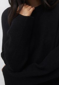 Pull en tricot noir surdimensionné avec une finition texturée. Manches longues et large décolleté pour un ajustement décontracté. Design minimaliste.