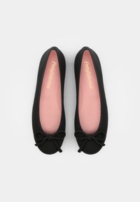 Paire de ballerines noires avec semelles roses et petits nœuds à l’avant, vues de dessus sur un fond uni.