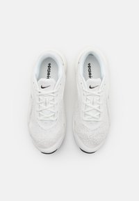 Scarpe da ginnastica bianche con parte superiore in tessuto a maglia, punta rotonda, suola nera a contrasto e logo nero con allacciatura tradizionale.